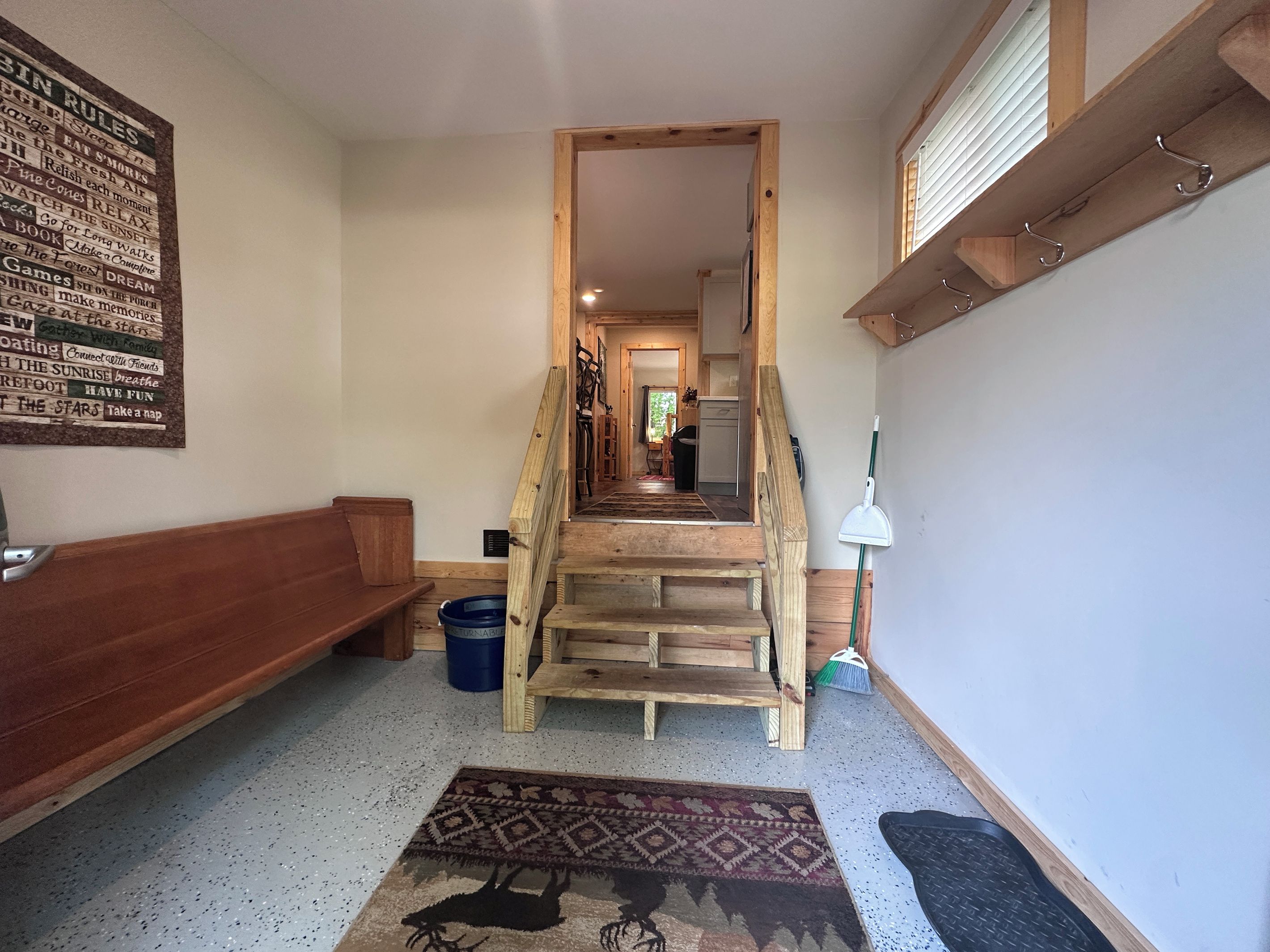 Eine Holztreppe führt zu einer zweiten Etage, ein blauer Eimer, ein gemustertes Teppich und eine Wand mit Text.