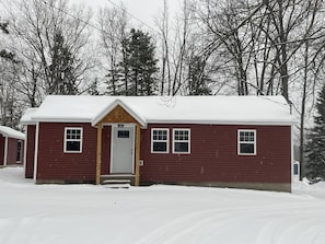 A red wooden house with a snow-covered roof and a front porch. - Private hot tub -2 king beds -near Pictured Rocks! (Christmas)