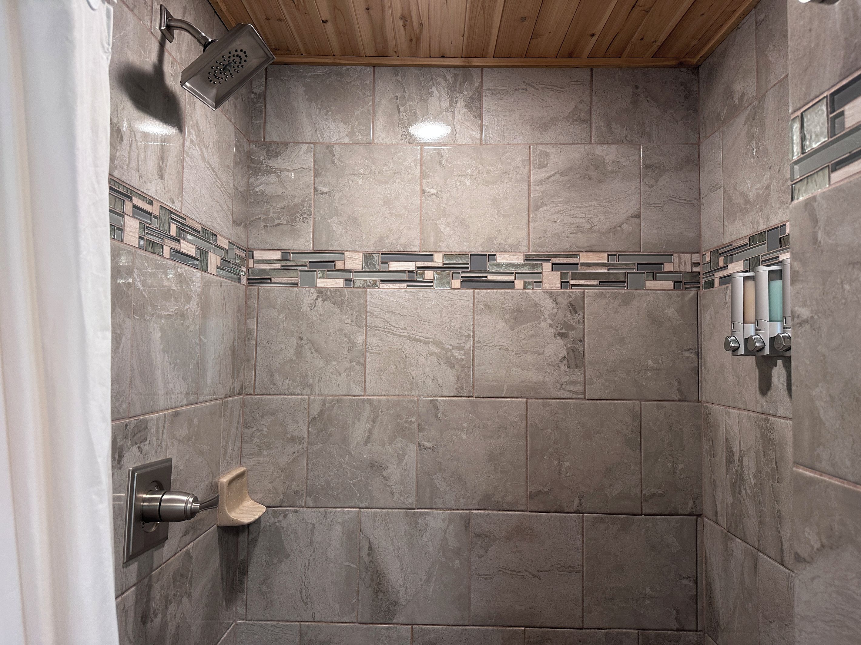 A shower with a wooden ceiling, tiled walls, and a hand shower.
