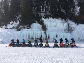 A group of people on snowmobiles in a snowy landscape with a large ice formation in the background. - Private hot tub -2 king beds -near Pictured Rocks! (Christmas)