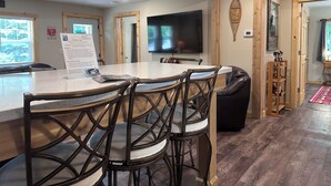 Een moderne keuken met een groot eiland, donkerhouten stoelen, een flatscreen televisie en een houten plafond.