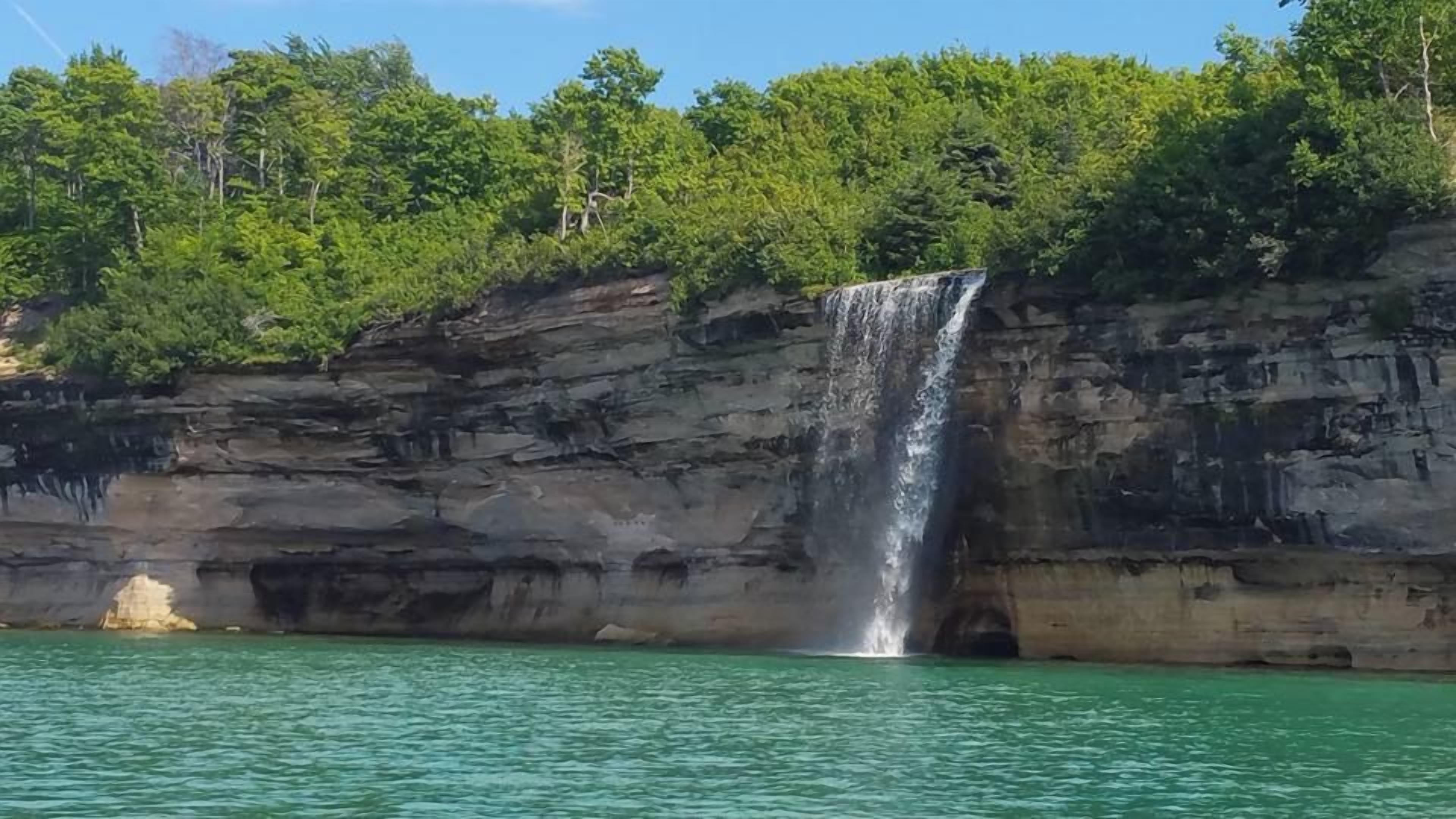 A waterfall cascading down a rocky cliff into a body of water, surrounded by dense green foliage.