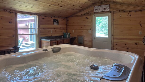 Een houten cabin interieur met een bubbelbad, houten wanden, een bordje met de tekst 'Ontmoet me onder de harsdoorn' en een deur met een raam.