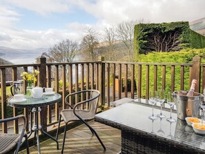 A deck with a table and chairs, a bottle of champagne, and a view of the countryside. - The Old Post Office on Loch Tay (Aberfeldy, near Loch Tay)