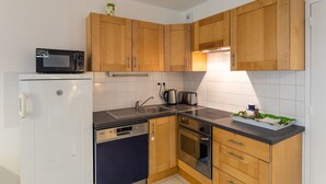 A compact kitchen with wooden cabinets, a microwave, a dishwasher, and a stove. - Le Bonnet Rouge - Appartement 2 chambres avec parking (Rennes)