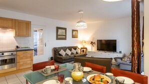A modern kitchen with wooden cabinets, a dining table set for breakfast, and a living area with a sofa and TV. - Le Bonnet Rouge - Appartement 2 chambres avec parking (Rennes)