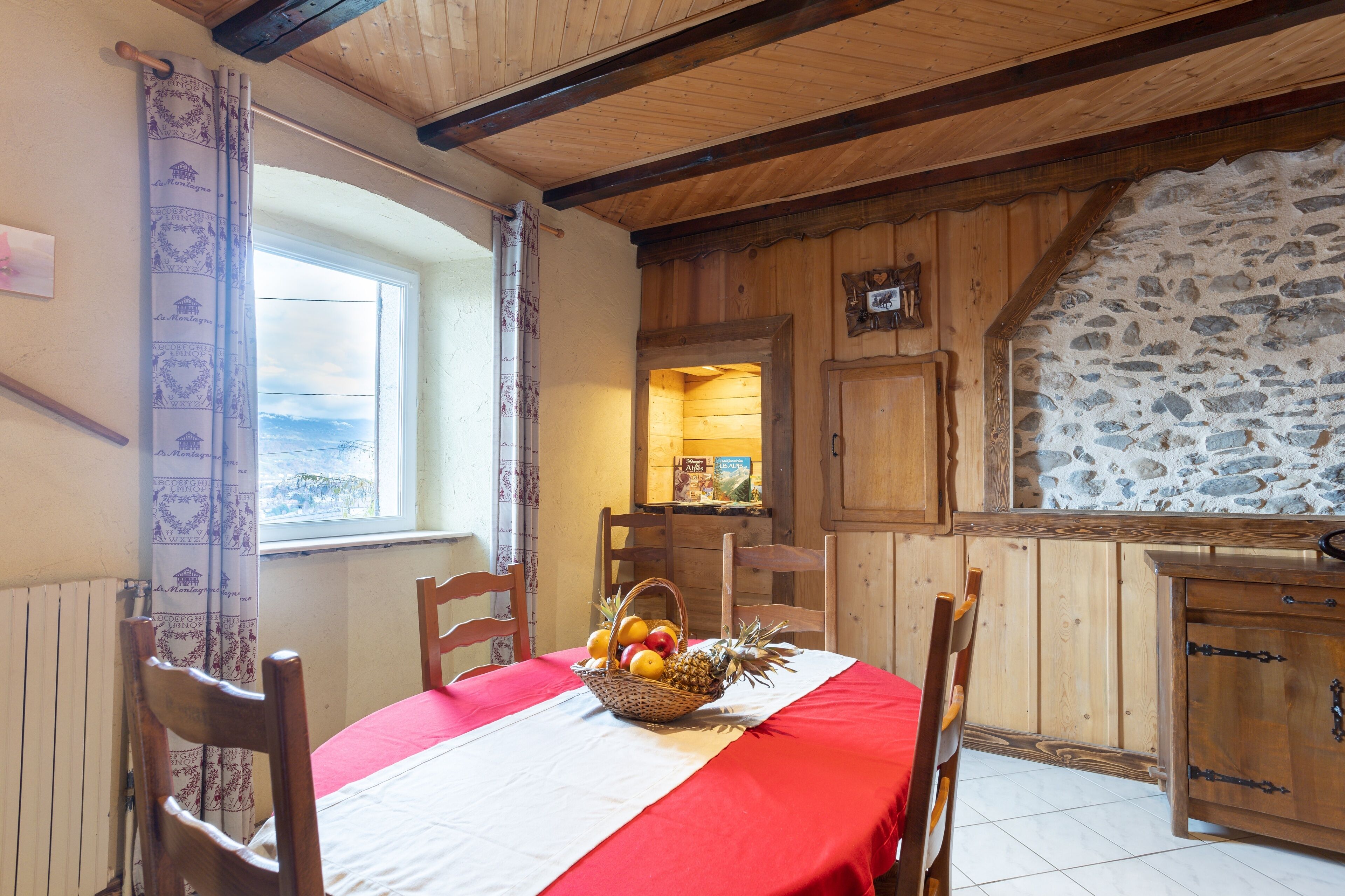 Un coin repas avec une table dressée pour deux personnes, un mur en pierre, des meubles en bois et une fenêtre offrant une vue agréable.