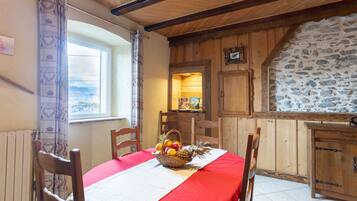 Un coin repas avec une table dressée pour deux personnes, un mur en pierre, des meubles en bois et une fenêtre offrant une vue agréable.