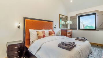 Une chambre moderne avec un grand lit, une table de chevet, une commode et une fenêtre donnant sur un paysage verdoyant.