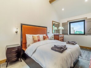 Een moderne slaapkamer met een groot bed, een nachtkastje, een dressoir en een raam met uitzicht op groen.