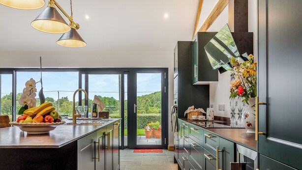 A modern kitchen with a large island, a view of greenery outside, and a dining area with a red mat.