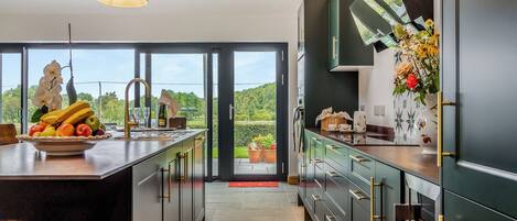 A modern kitchen with a large island, a view of greenery outside, and a dining area with a red mat.