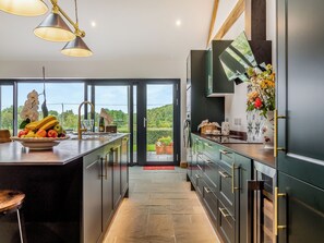 A modern kitchen with a large island, a view of greenery outside, and a dining area with a red mat. - 3 bedroom accommodation in Watton (Watton)