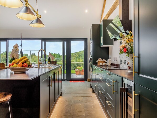 A modern kitchen with a large island, a view of greenery outside, and a dining area with a red mat.