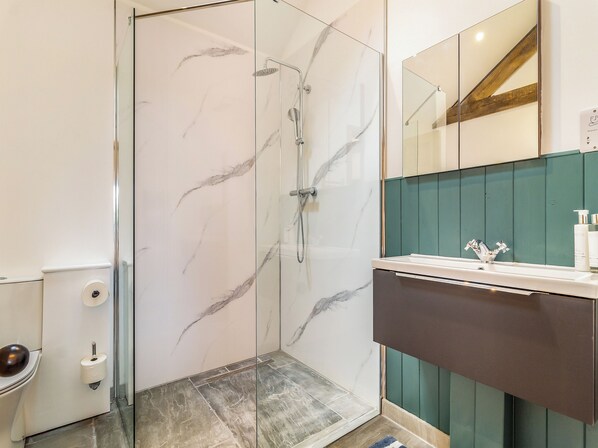 A bathroom with a glass-enclosed shower, a toilet, and a sink with a mirror above it.
