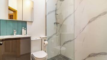 Un baño moderno con ducha de vidrio, inodoro y tocador con espejo y encimera.