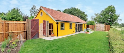 Una casa amarilla con techo de tejas rojas, patio cercado y terraza de madera.