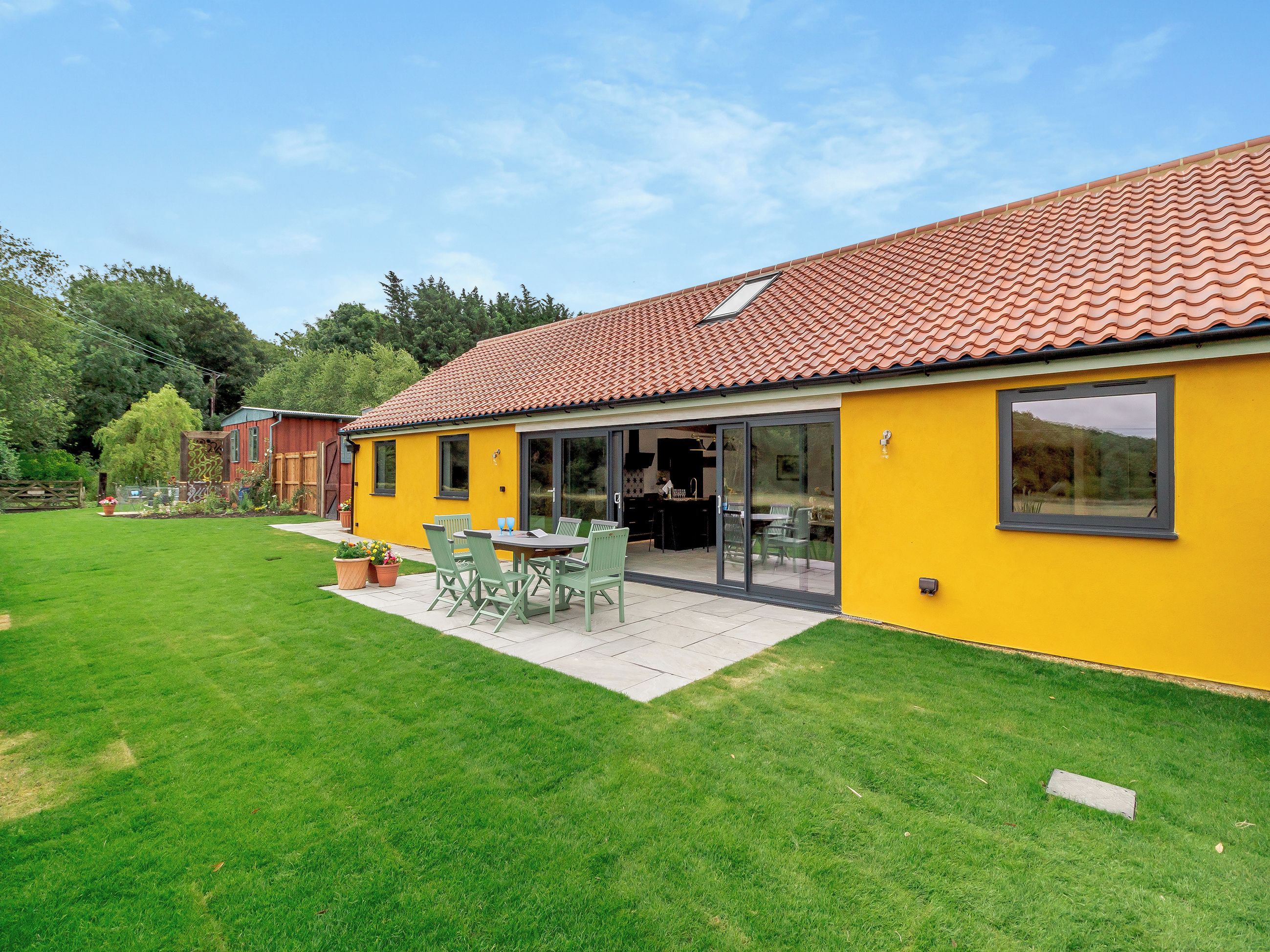 Ein gelbes Gebäude mit einem Ziegeldach, einer Terrasse mit Gartenmöbeln und einem gepflegten Rasen.