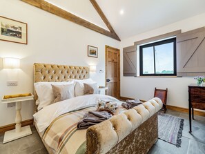 A bedroom with a tufted headboard, a large window, a wooden bench, and a bedside table with a lamp. - 3 bedroom accommodation in Watton (Watton)