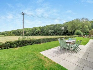 Une terrasse avec une table et des chaises, une pelouse bien entretenue et une haie.