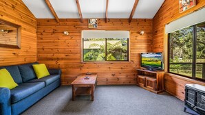 A cozy cabin interior with a wooden interior, a sofa, a coffee table, a television, and a window with a view of greenery.