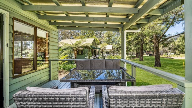 A covered patio with wicker furniture, a view of a garden with a gazebo, and a house in the background.