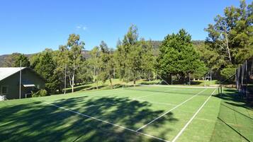 Un campo da tennis con una rete, circondato da alberi e un edificio.
