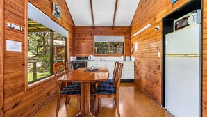 A wooden cabin interior with a dining table, chairs, a kitchen area, and a refrigerator.