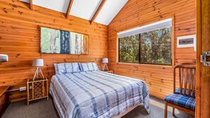 A cozy bedroom with a bed, two bedside lamps, a window with a view of trees, and a wooden floor.
