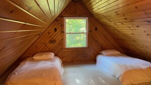 A small, wooden-paneled attic bedroom with two single beds, a window, and a sloped ceiling.