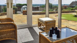 A room with a large glass door leading to a patio with a wicker chair, a small table, and binoculars on the table. - A spacious and well presented bungalow with amazing views over Berkshire. (Reading)