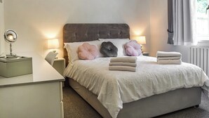 A neatly made bed with a white duvet, a bedside lamp, and a mirror on a nightstand. - A spacious and well presented bungalow with amazing views over Berkshire. (Reading)