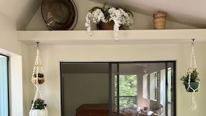 Une pièce dotée d’une porte-fenêtre coulissante donnant sur un balcon, d’un banc en bois, d’une chaise de réalisateur et de jardinières suspendues.