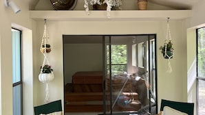 Une pièce dotée d’une grande porte-fenêtre coulissante donnant sur un balcon, de deux chaises pliantes, d’un panier en osier et d’un ventilateur de plafond.