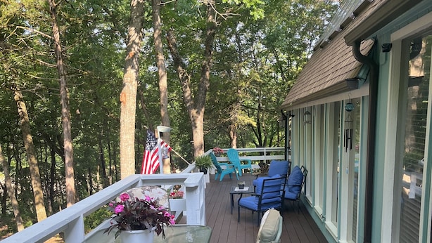 Une terrasse couverte avec une table en verre, des chaises et un banc. On y trouve également un drapeau et un paillasson.