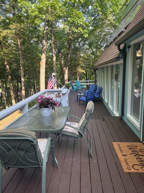 A covered deck with a glass table, chairs, and a bench. There is a flag and a welcome mat. - Large unique home in the beautiful Ozark Mountains on the Kings River. (Berryville)