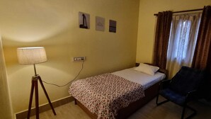 A small, single-bed room with a bedside lamp, a chair, and a mirror. - 2BR Apartment in the heart of Guwahati (Guwahati)