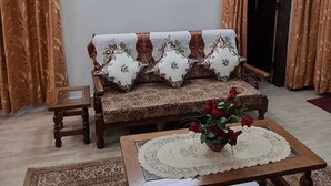 A living room with a sofa, a coffee table with a vase of flowers, a ceiling fan, and patterned curtains. - 2BR Apartment in the heart of Guwahati (Guwahati)