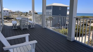 Un espace extérieur abrité doté d’une terrasse en bois, de mobilier blanc et offrant une vue sur la plage et l’océan.