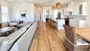Une cuisine moderne avec des meubles blancs, un îlot central et un coin repas comprenant une banquette et des chaises.
