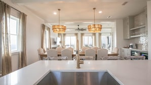 Une cuisine moderne avec des meubles blancs, un îlot central doté d’un évier et des luminaires suspendus.