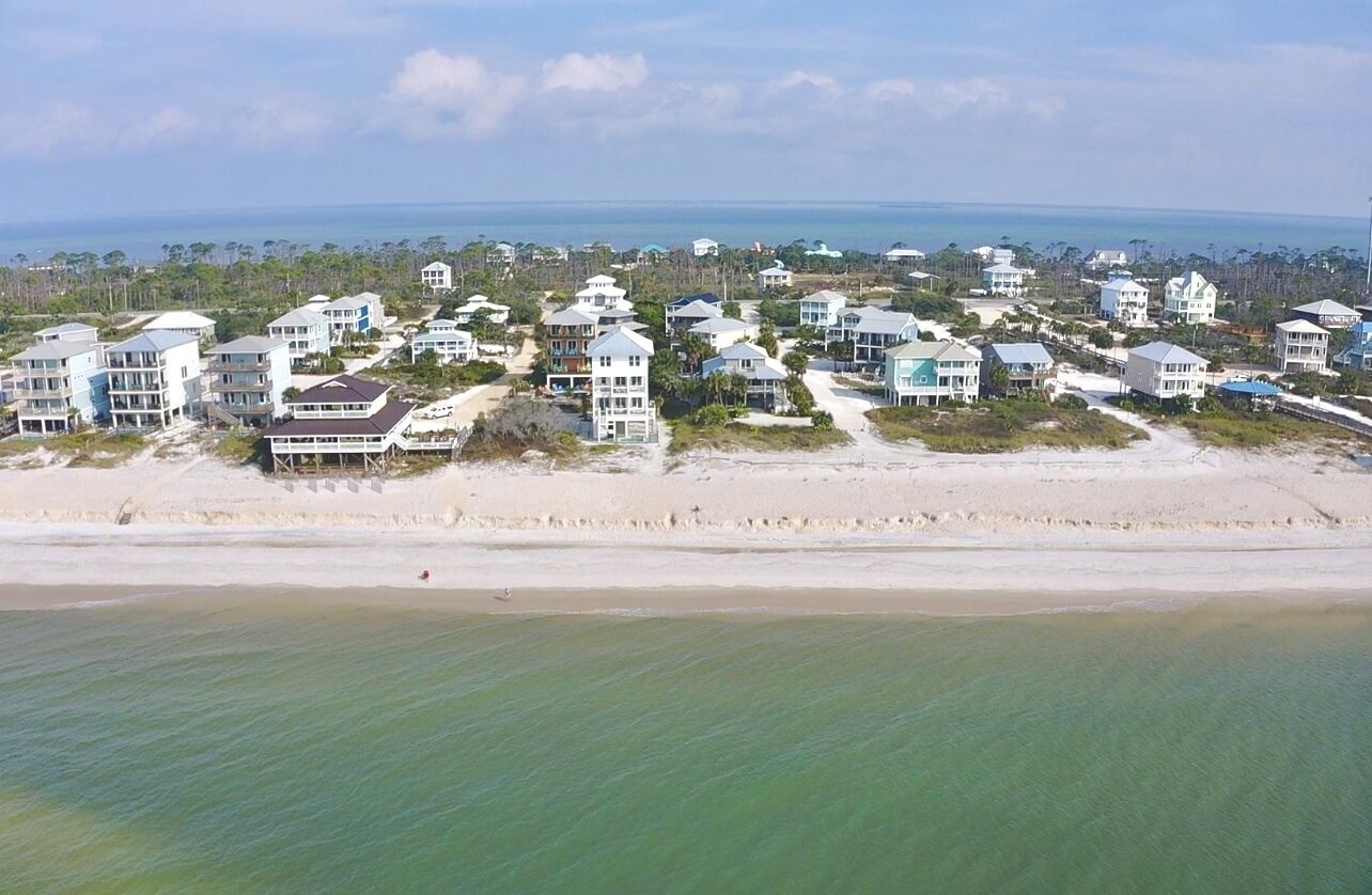 A coastal residential area with beachfront properties, including multi-story houses and villas, with a clear view of the ocean and beach.
