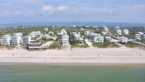 Un quartier résidentiel situé sur la côte, avec des propriétés en bord de mer, notamment des maisons à plusieurs étages et des villas, donnant sur une plage de sable et l’océan.