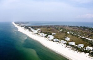 Vista aérea de una zona costera con playa, casas y una línea de costa distante.