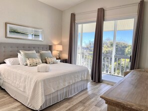Ein Schlafzimmer mit einem großen Bett, einem Nachttisch mit Lampe, einer hölzernen Bank und einem Balkon mit Vorhängen.