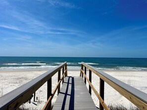 Ein hölzerner Steg führt zu einem Strand bei klarem Himmel.