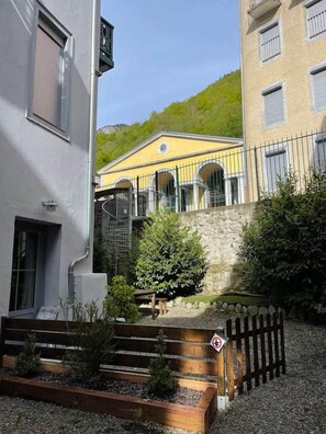 A courtyard with a yellow building, a stone wall, and a wooden fence. - Le Tavae (Cauterets)