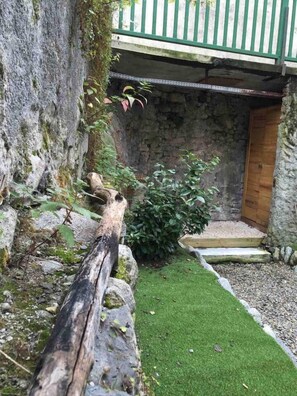 A stone wall with a wooden door, a small grassy area, and a wooden fence.