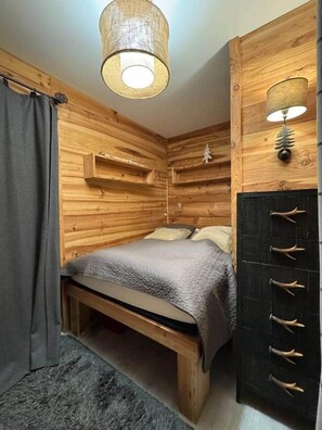A wooden room with a bed, a wall-mounted cabinet, and a hanging light fixture.