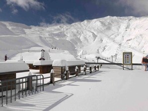 Ein schneebedecktes Skigebiet mit Holzhütten, einer Seilbahn und einem Berg im Hintergrund.